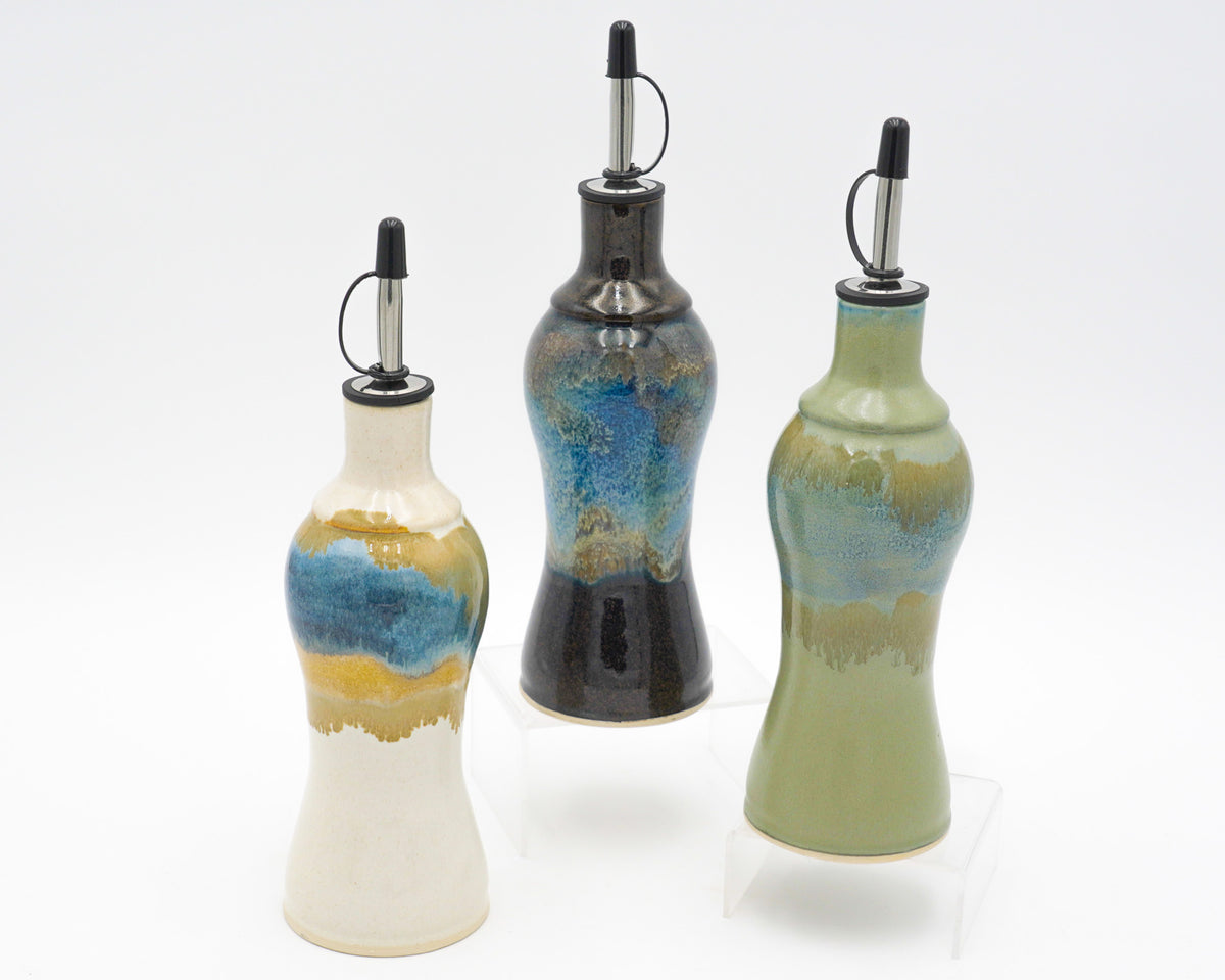 Three ceramic oil bottles with decorative glaze on a white background