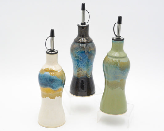 Three ceramic oil bottles with decorative glaze on a white background