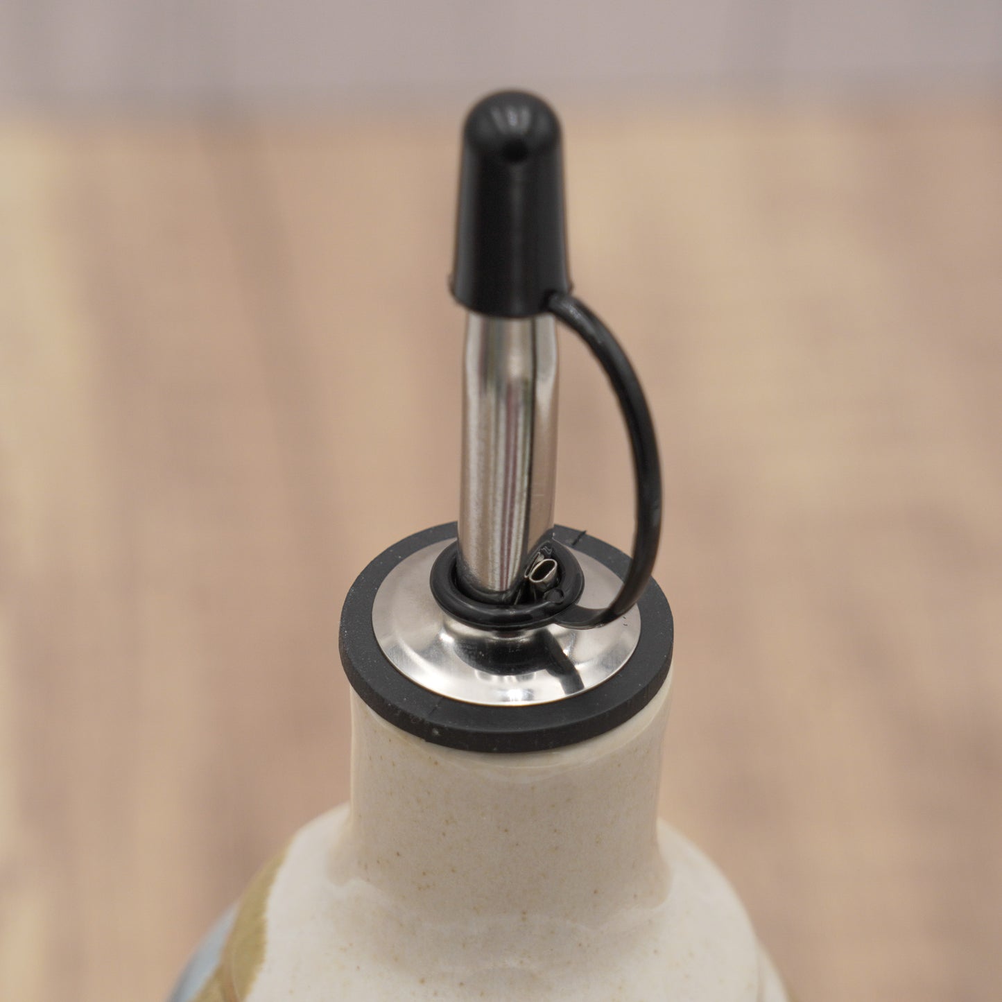 Close-up of a white ceramic bottle with a metal and silicone pourer that has a black cap 