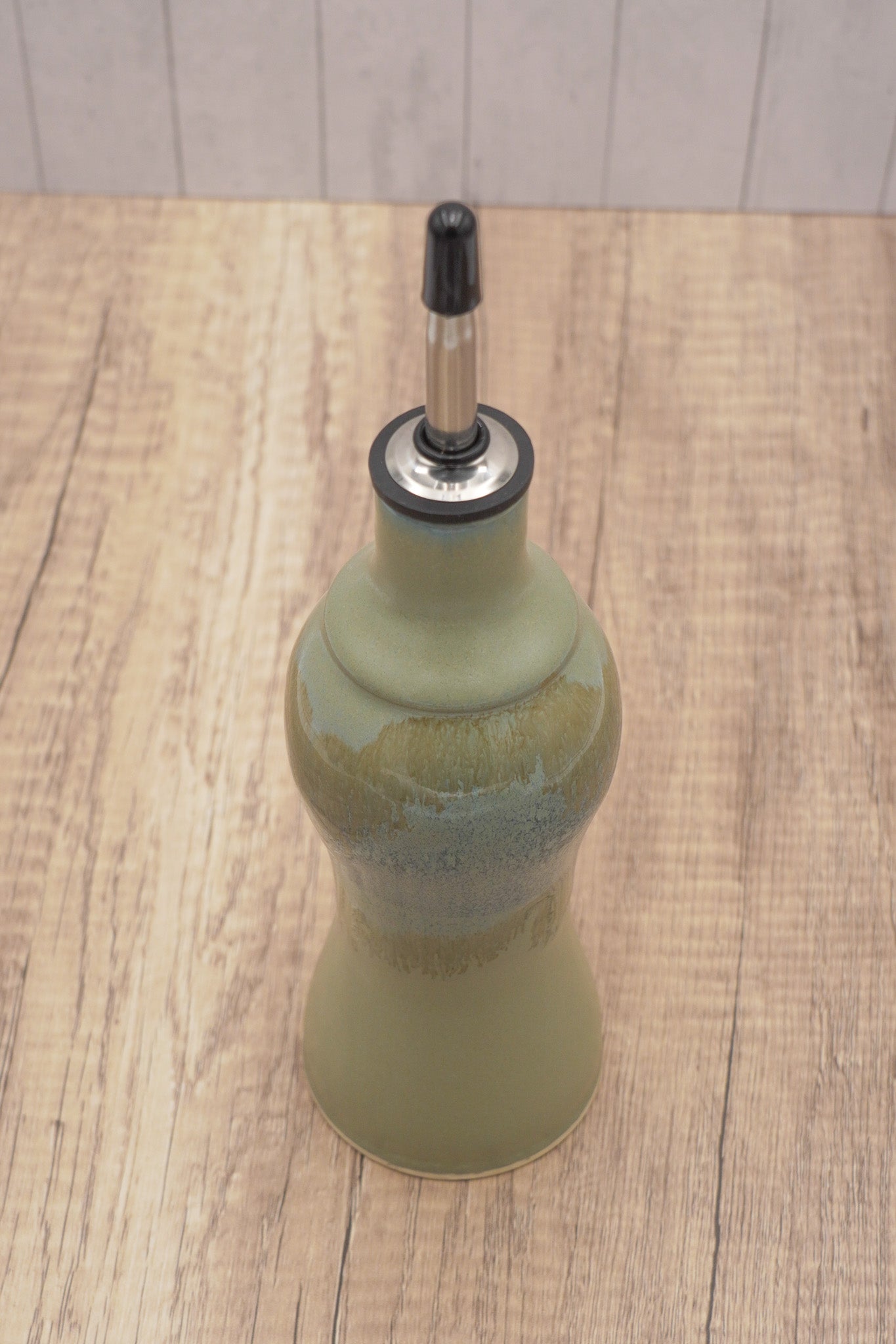 Green ceramic bottle with black cap on a wooden surface
