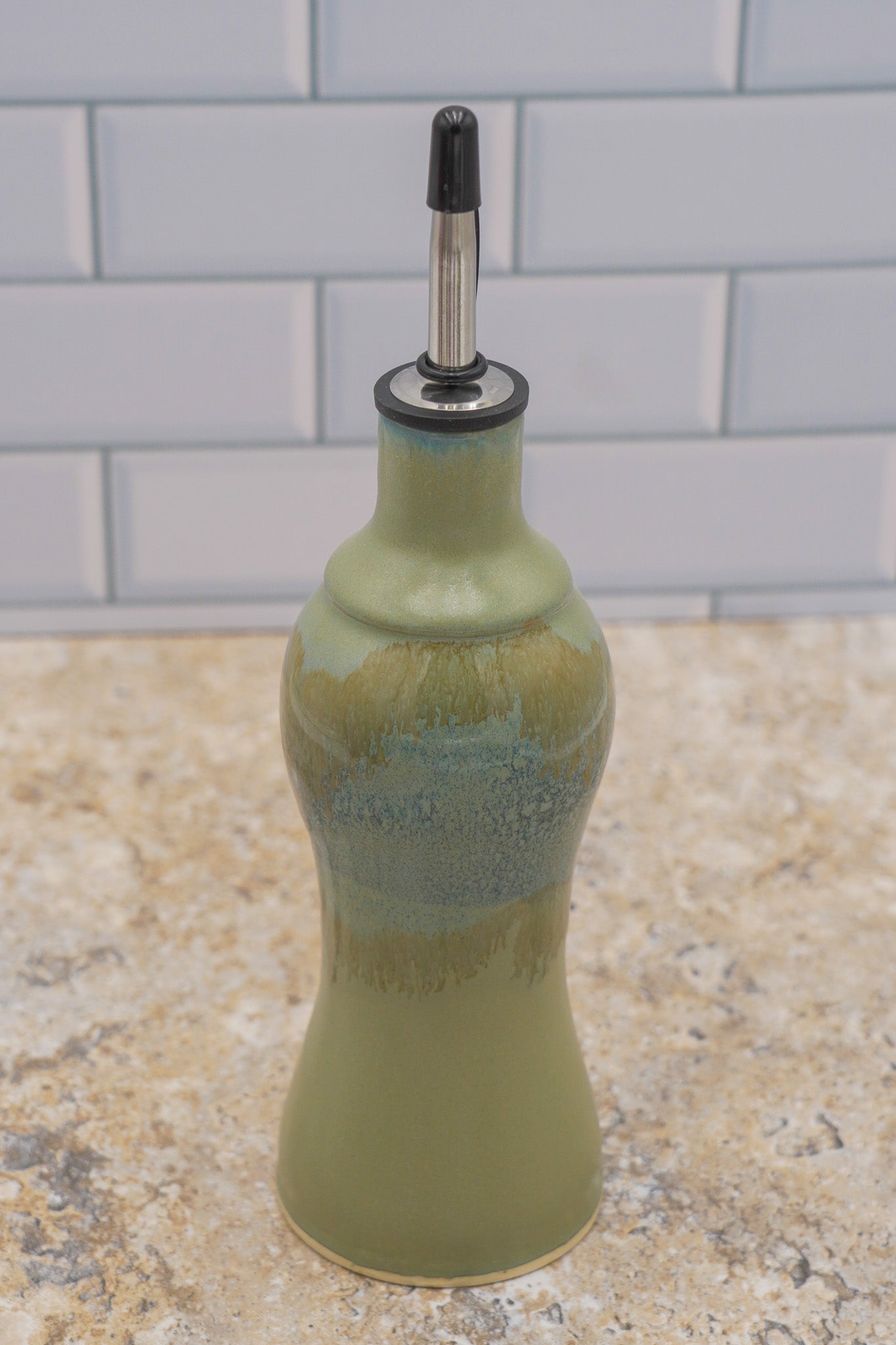 Green ceramic olive oil bottle with a black cap on a kitchen counter.